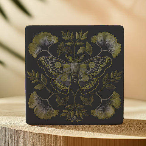 Square black ceramic coaster featuring a detailed chartreuse luna moth illustration surrounded by symmetrical botanical elements including ginkgo-inspired leaves and delicate foliage.